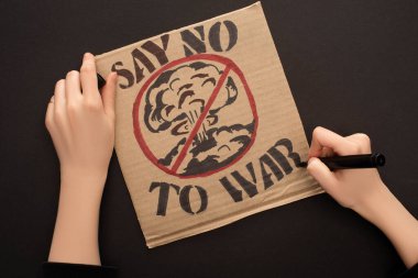 cropped view of woman drawing placard with say no to war lettering on black background clipart