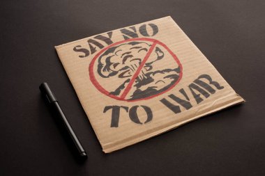 marker near cardboard placard with say no to war lettering and explosion in stop sign on black background clipart