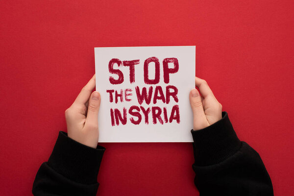 partial view of woman holding white placard with stop war in Syria lettering on red background