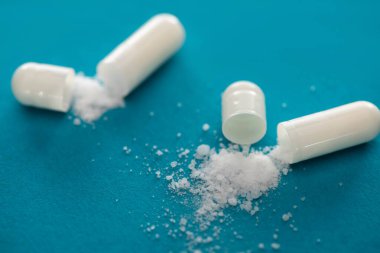 mavi arkaplanda beyaz toz bulunan probiyotik kapsüllerin seçici odak noktası