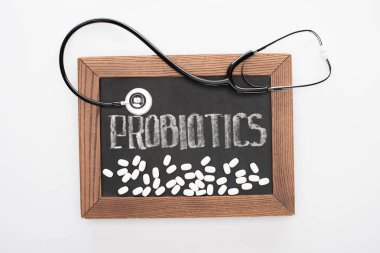 top view of chalkboard with probiotics lettering with pills and stethoscope on white background clipart