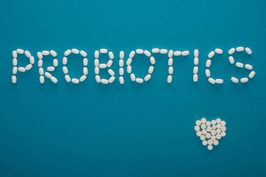 Probiyotik yazıtlarının üst görüntüsü ve mavi arka plandaki haplardan yapılmış kalp.