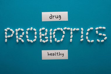 top view of probiotics lettering made of pills near paper cards with healthy and drug words on blue background clipart