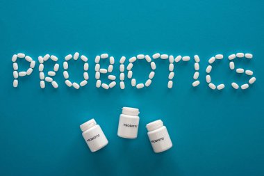 top view of probiotics lettering made of pills and containers on blue background clipart
