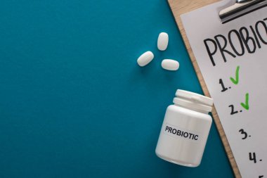 Probiyotikleri boş olan panonun mavi arka planda hapları olan konteynırın yanındaki boş listenin üst görünümü