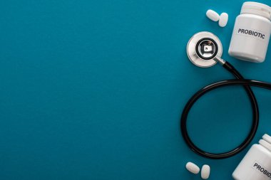 Mavi arka planda probiyotik harfleri, hapları ve steteskopu olan konteynırların üst görünümü