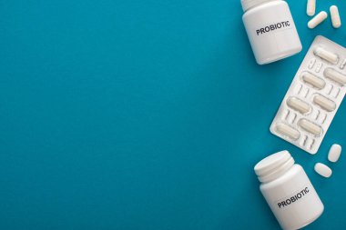 Probiyotik harfli konteynırların üst görünümü, mavi arka planda haplar ve kabarcık paketi