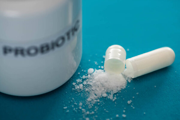 selective focus of probiotic container near capsule with white powder on blue background