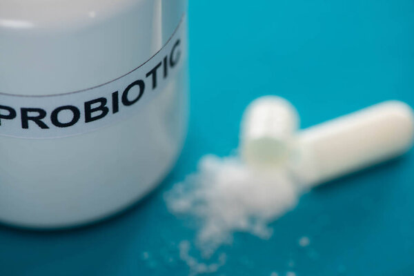 selective focus of probiotic container near capsule with white powder on blue background