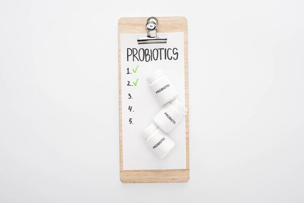 top view of clipboard with probiotics empty list and pills on white background
