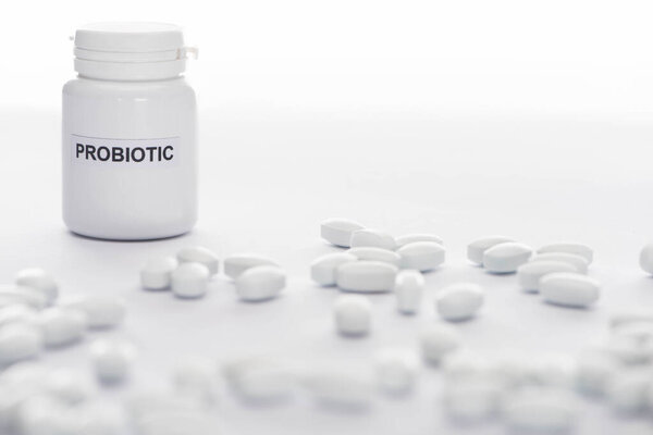 selective focus of probiotic container near pills on white background