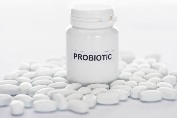 selective focus of probiotic container near pills on white background