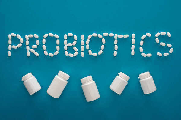 top view of probiotics lettering made of pills and white containers on blue background