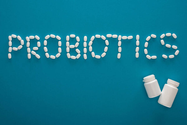 top view of probiotics lettering made of pills and containers on blue background