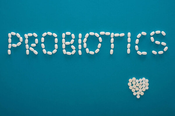top view of probiotics lettering and heart made of pills on blue background