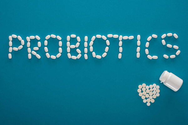 top view of probiotics lettering and heart made of pills and container on blue background