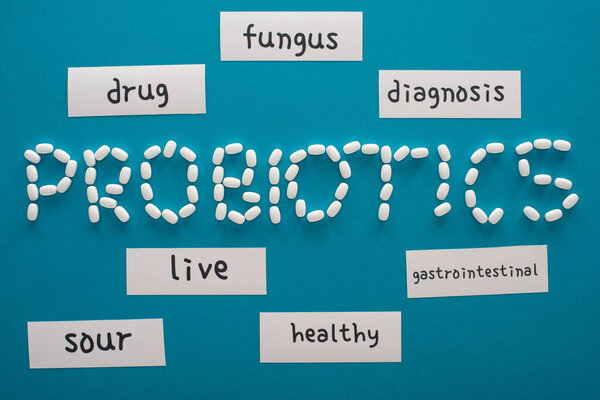 top view of probiotics lettering made of pills near paper cards with words on blue background