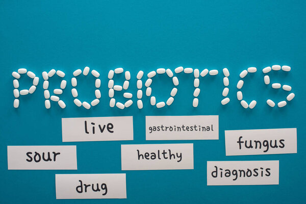 top view of probiotics lettering made of pills near paper cards with words on blue background