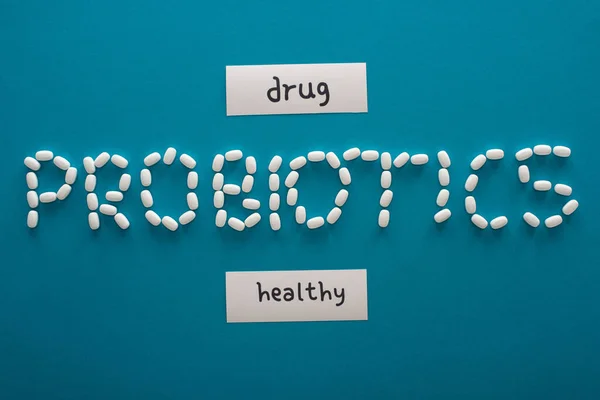 青の背景に健康と薬物の単語を持つ紙のカードの近くに丸薬で作られたプロバイオティクスのレタリングのトップビュー — ストック写真