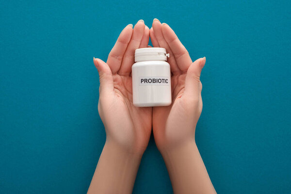 cropped view of woman holding white probiotic container in hands on blue background