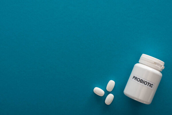 top view of white probiotic container with pills on blue background