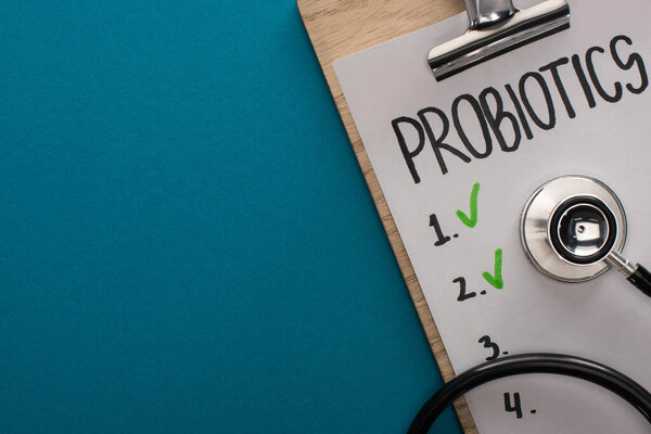 top view of clipboard with probiotics empty list and stethoscope on blue background