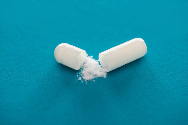 close up view of probiotic capsule with white powder on blue background