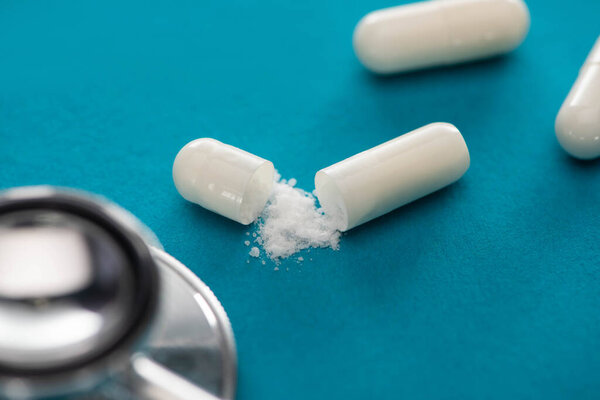 close up view of probiotic capsules with white powder and stethoscope on blue background
