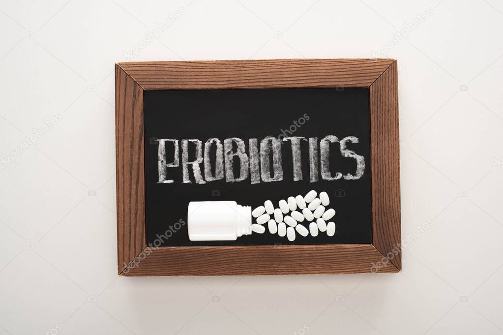 top view of chalkboard with probiotics lettering with pills and container on white background