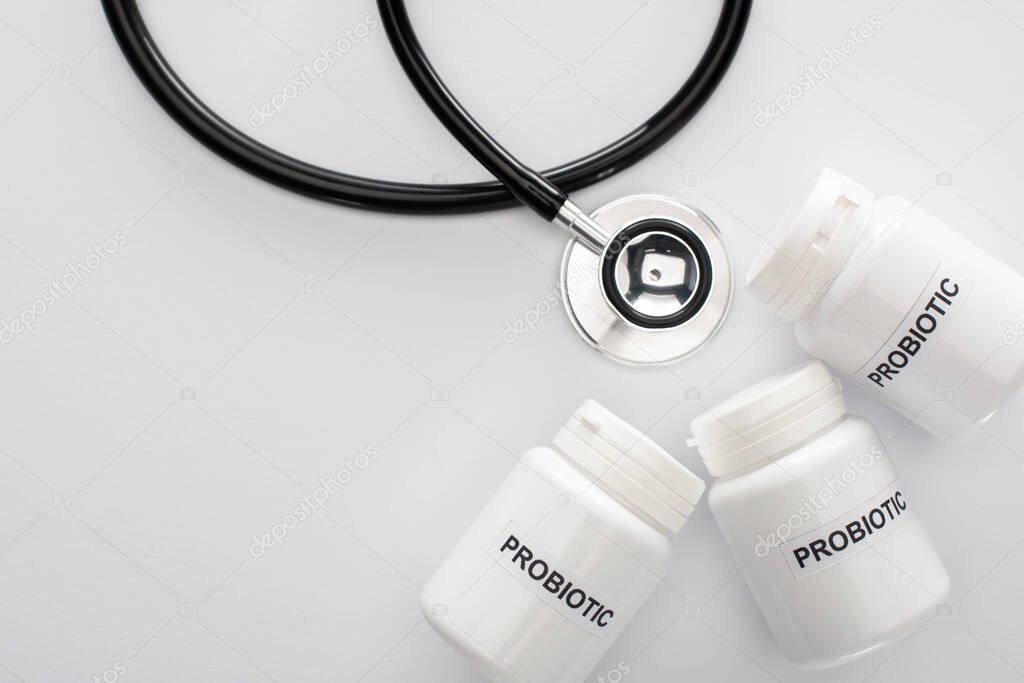 top view of containers with probiotic lettering near stethoscope on white background