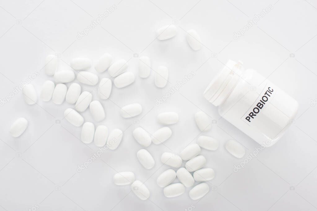 top view of container with probiotic lettering near pills on white background