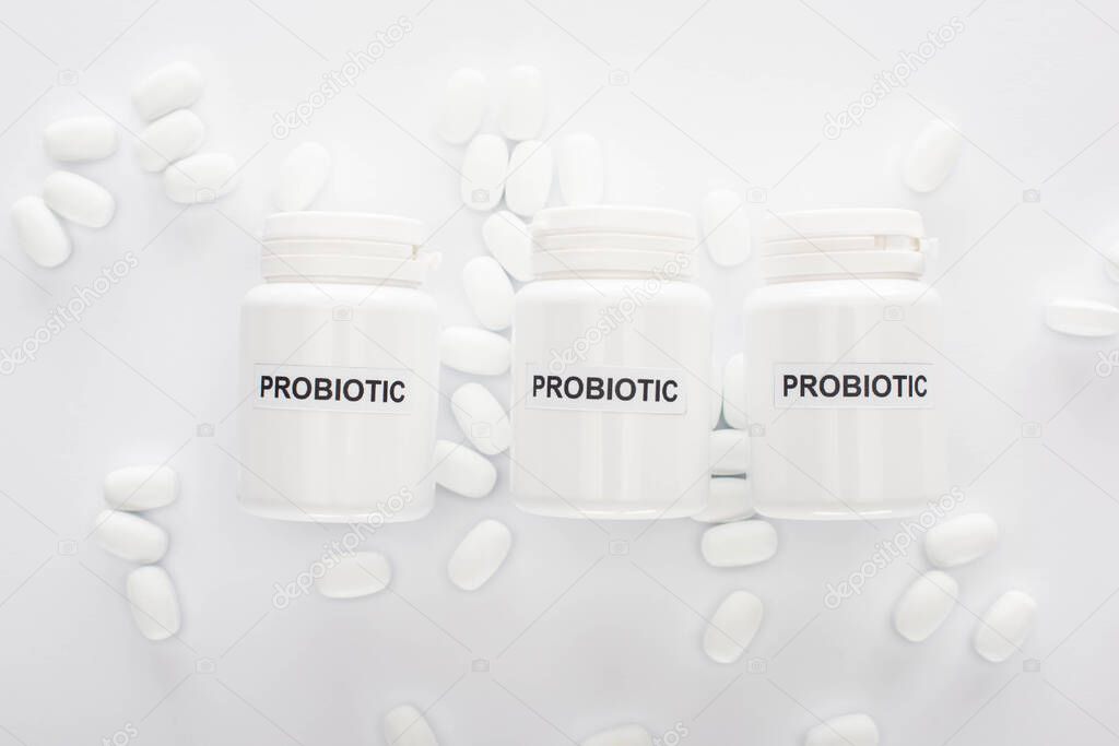 top view of containers with probiotic lettering near pills on white background