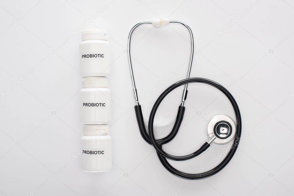 top view of containers with probiotic lettering near stethoscope on white background