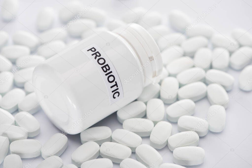 selective focus of probiotic container near pills on white background