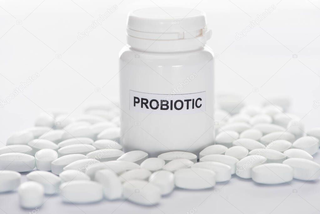 selective focus of probiotic container near pills on white background