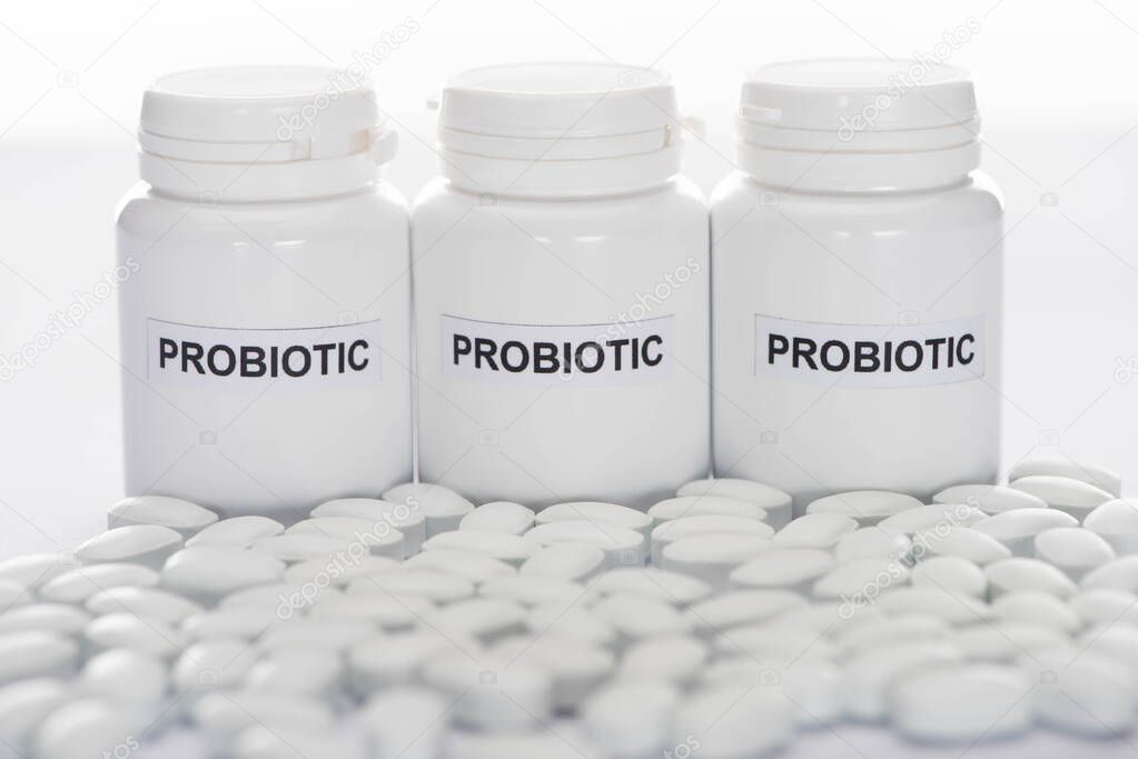 selective focus of probiotic containers near pills on white background