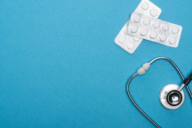 Su toplayan hapların üst görüntüsü ve mavi arka planda steteskop.