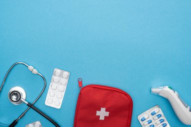 top view of pills in blister packs, stethoscope, first aid kit and ear thermometer on blue background clipart