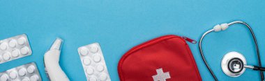 top view of pills in blister packs, stethoscope, first aid kit and ear thermometer on blue background, horizontal image clipart