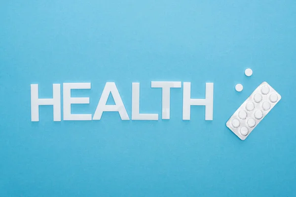 ブリスターパックの丸薬のトップビューと青い背景の健康レタリング — ストック写真