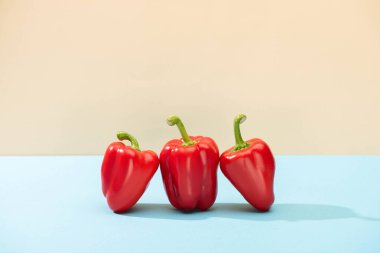 fresh red bell peppers on blue surface isolated on beige clipart