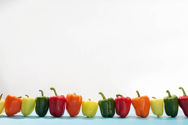 fresh colorful bell peppers in row on blue surface on white background