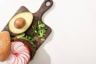 Turp, avokado ve ahşap kesim tahtasıyla beyaz arka planda lezzetli vejetaryen hamburgerinin üst görüntüsü.