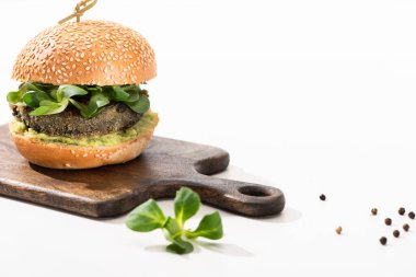 delicious green vegan burger with microgreens, black pepper on wooden cutting board on white background clipart