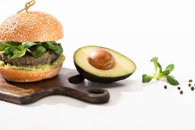 Lezzetli yeşil vegan burger, mikroyeşillik, avokado, ahşap kesme tahtasında siyah biber beyaz arka planda.