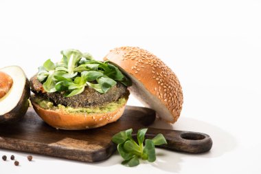 Lezzetli yeşil vegan burger, mikroyeşillik, avokado, ahşap kesme tahtasında siyah biber beyaz arka planda.