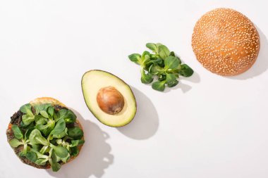 Avokadolu vejetaryen burgerin üst görüntüsü ve beyaz arka planda mikroyeşiller