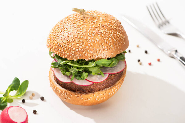 selective focus of delicious vegan burger with radish and arugula with black pepper on white background