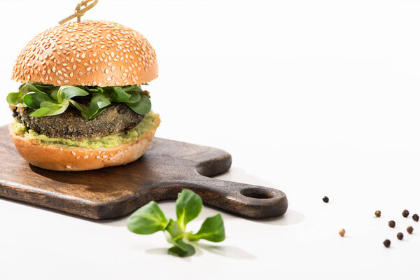delicious green vegan burger with microgreens, black pepper on wooden cutting board on white background