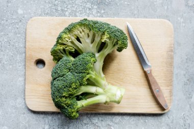 top view of fresh green cut broccoli on wooden cutting board with knife on grey surface clipart